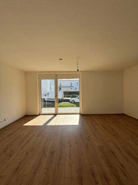Geräumiges Wohnzimmer mit Holzboden und Zugang zu einem Balkon oder einer Terrasse, sonnendurchflutet.