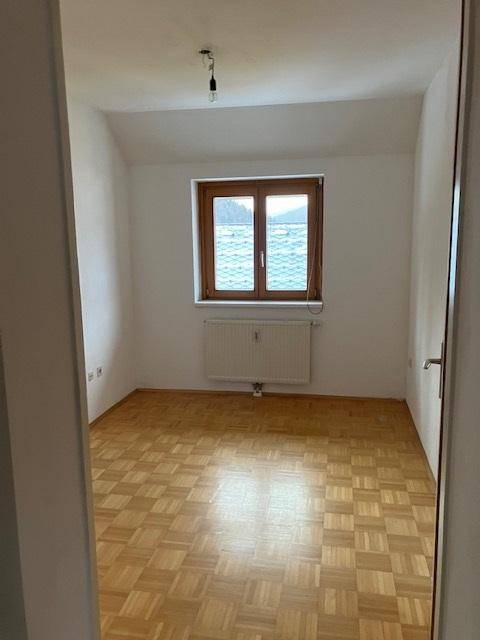Helles Schlafzimmer mit Parkettboden und einem Fenster mit Blick ins Grüne.
