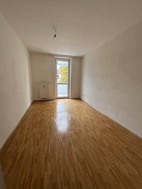 Geräumiges Zimmer mit hellem Parkettboden und Zugang zu einem französischen Balkon.