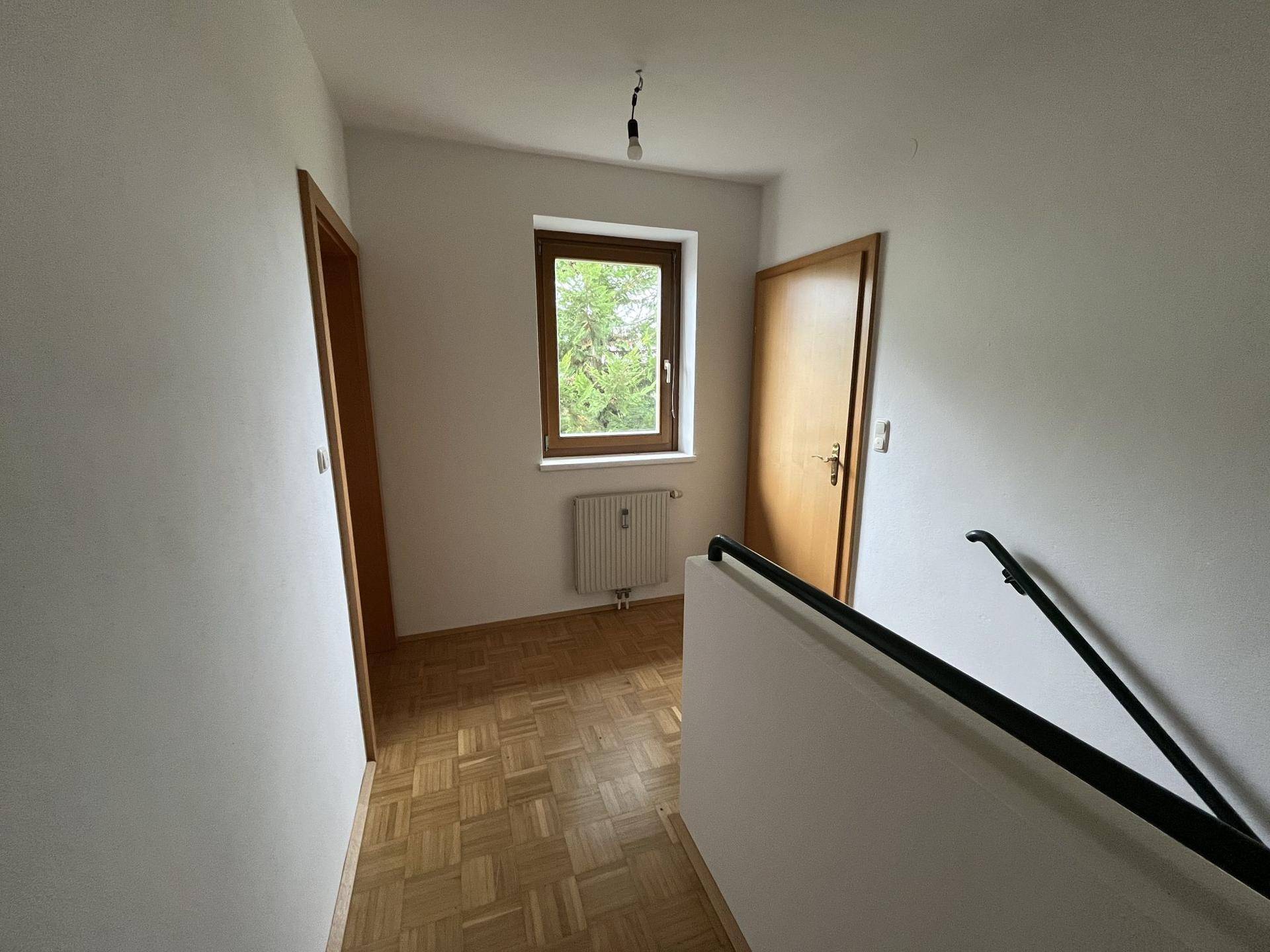 Heller Flurbereich im Obergeschoss mit Parkettboden, Fenster und Zugang zu weiteren Zimmern.