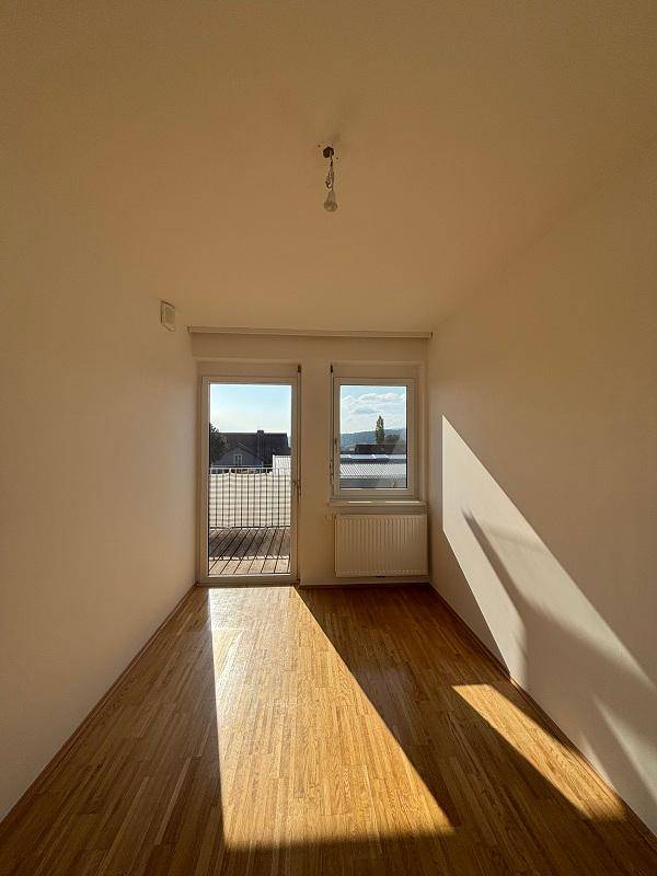 Lichtdurchfluteter Raum mit Holzboden und Balkonzugang, ideal für Wohn- oder Schlafbereich.