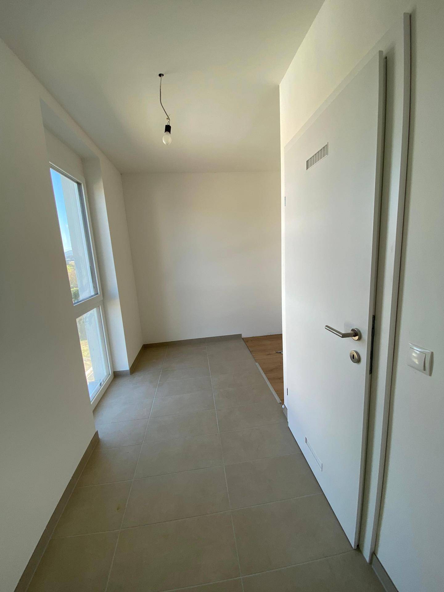 Heller Eingangsbereich mit Fliesenboden und einem Fenster, das viel Tageslicht hereinlässt.