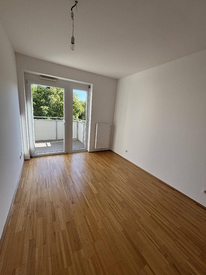 Helles Schlafzimmer mit Parkettboden und Balkonzugang, bietet viel natürliches Licht und frische Luft.