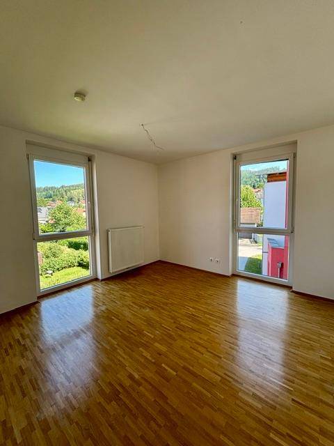 Helles Zimmer mit Parkettboden und zwei Fenstern, die einen Ausblick auf die Umgebung bieten.