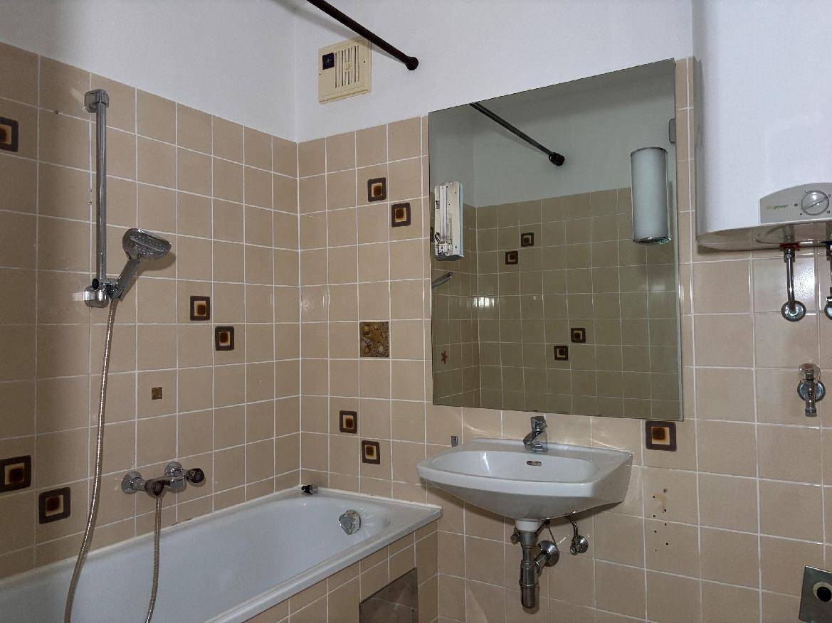 Badezimmer mit Badewanne, Waschbecken und Spiegel, ausgestattet mit beigen Fliesen.