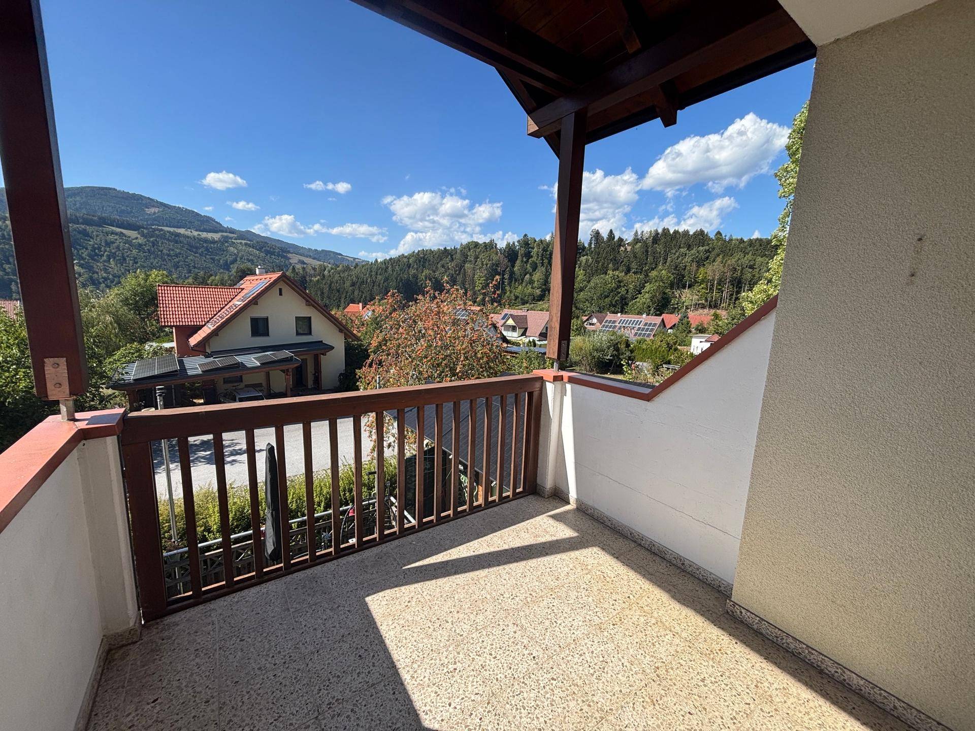 Geräumiger Balkon mit Holzgeländer und weitem Blick auf Berge und grüne Landschaft.