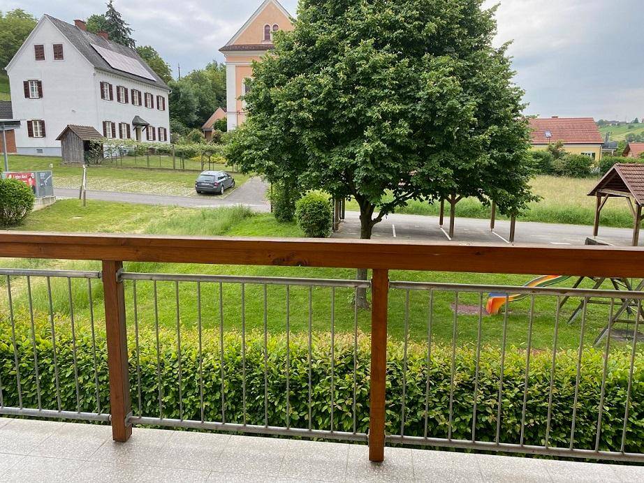 Blick vom Balkon auf eine grüne Umgebung mit Bäumen und einem Spielplatz.