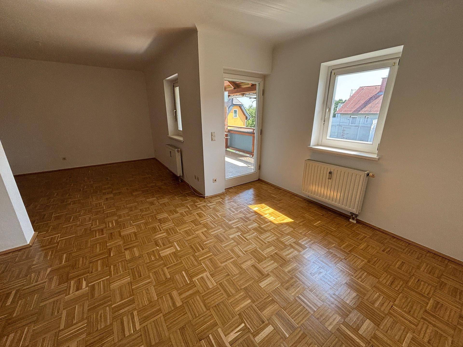 Heller Wohnraum mit Parkettboden, großem Fenster und Zugang zu einem Balkon.