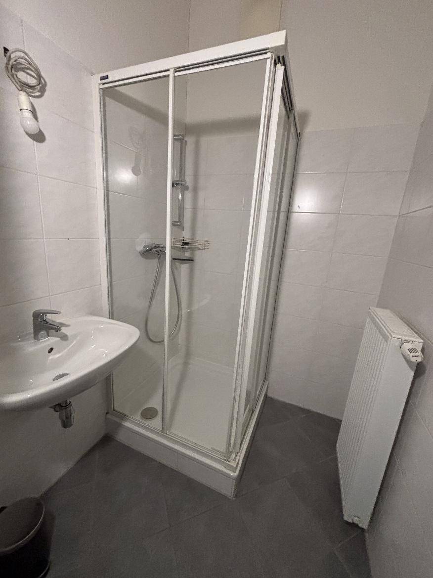 Badezimmer mit Duschkabine, Waschbecken und weißen Wandfliesen.