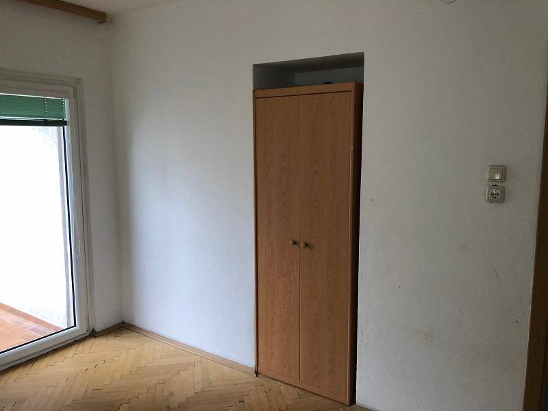 Leeres Zimmer mit Parkettboden, Balkonzugang und Einbauschrank.