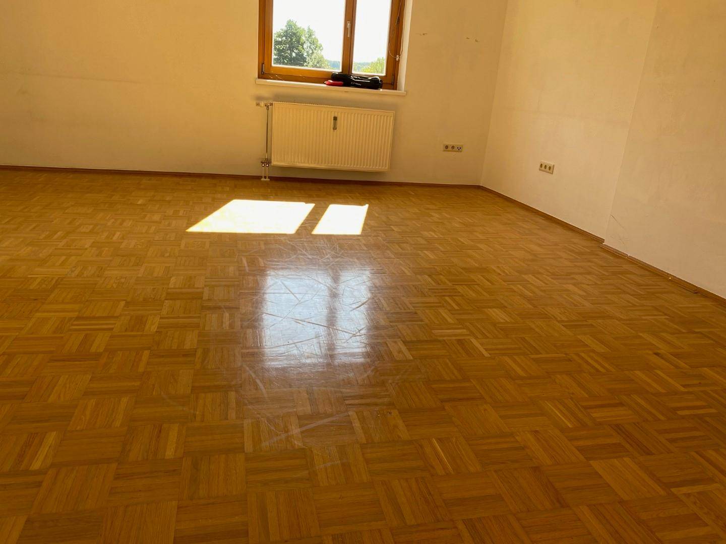 Heller Raum mit Parkettboden und einem Fenster, das viel Tageslicht hereinlässt.