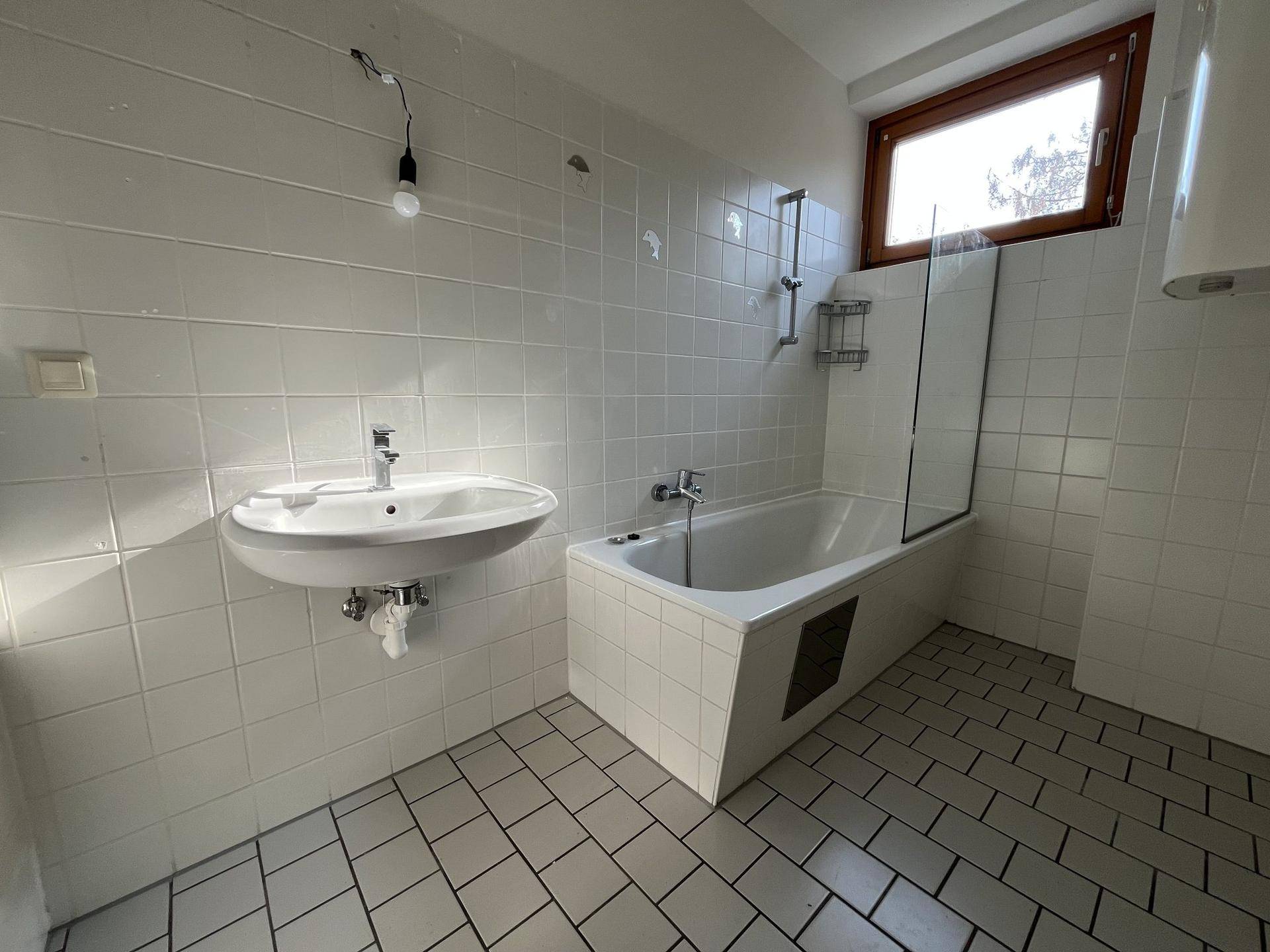 Funktionales Badezimmer mit Badewanne, Waschbecken und Fenster, hell gefliest.