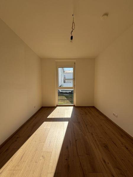 Helles Schlafzimmer mit Holzboden und einem großen Fenster, das viel Sonnenlicht hereinlässt.