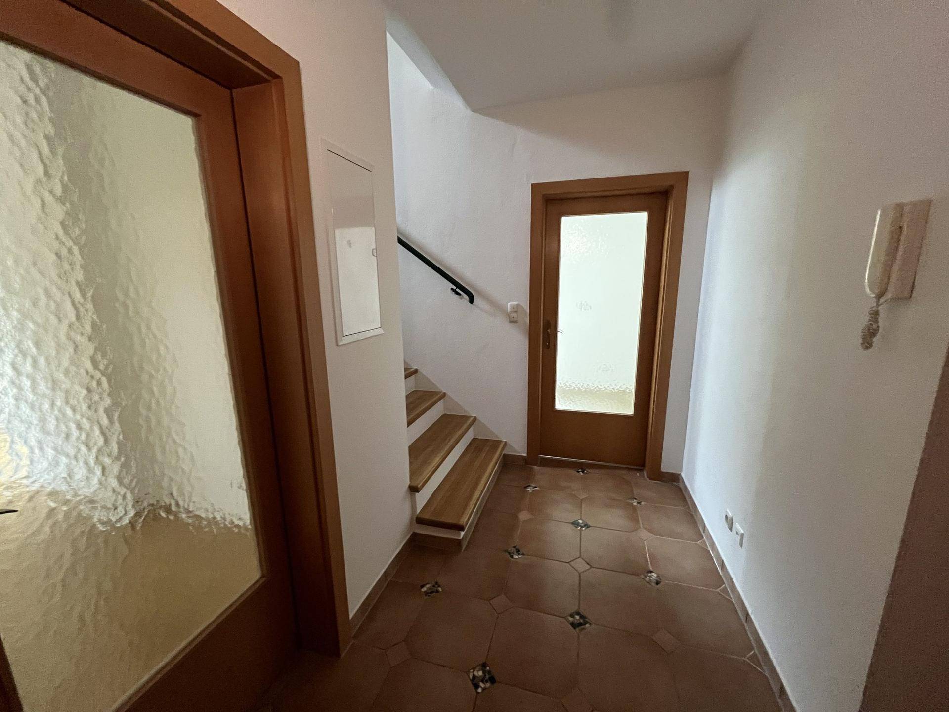 Heller Flur mit Terrakotta-Fliesenboden, Holztüren und Blick auf den Treppenaufgang.