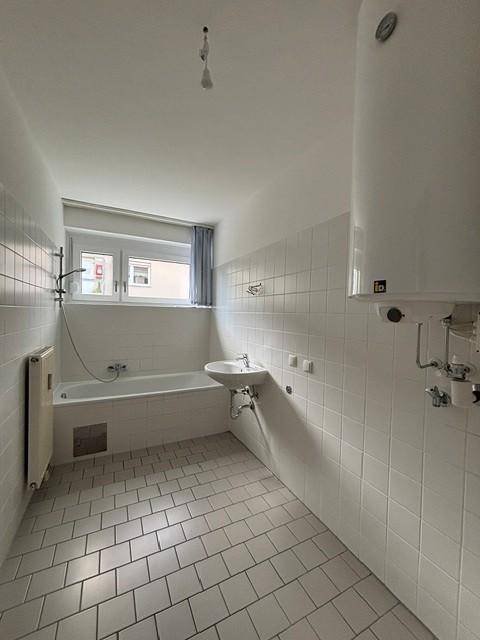 Helles Badezimmer mit Badewanne, Waschbecken und weißen Fliesen, inklusive Fenster.