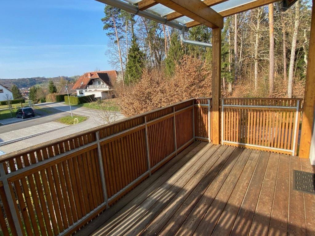 Geräumiger Holzbalkon mit Glasdach und Blick ins Grüne, ideal zum Entspannen.