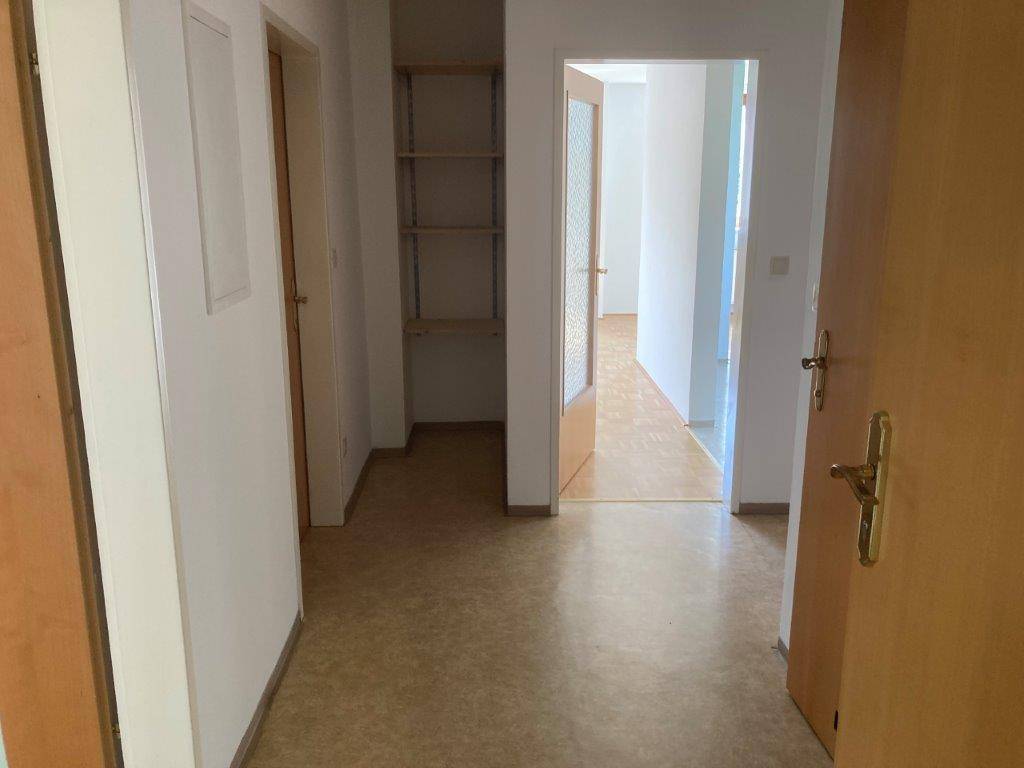 Flur mit Linoleumboden und offenen Regalen, der zu weiteren Räumen führt.