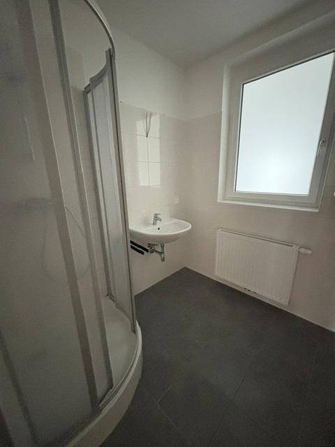 Modernes Badezimmer mit Duschkabine, Waschbecken und Fenster für natürliche Belüftung.