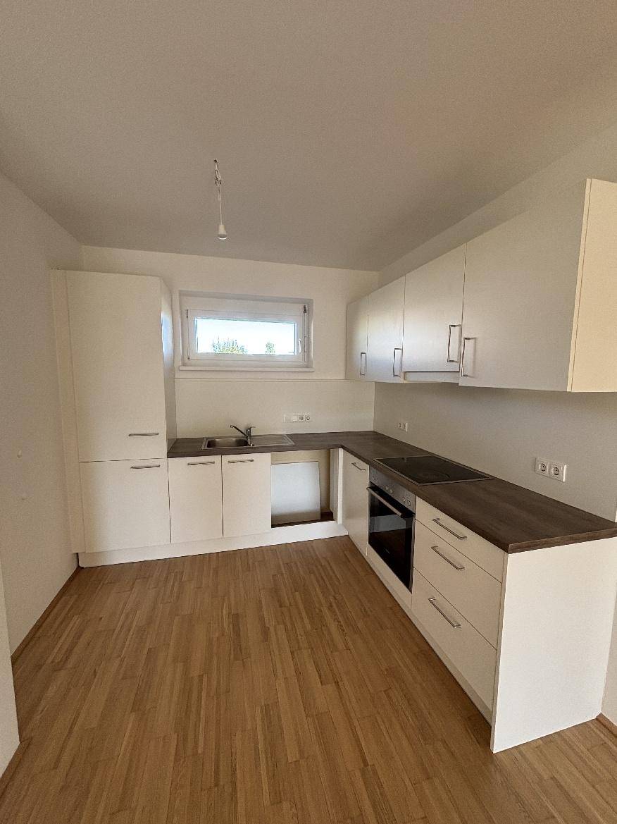 Moderne Küche mit weißen Schränken, Holzarbeitsplatte und Fenster.