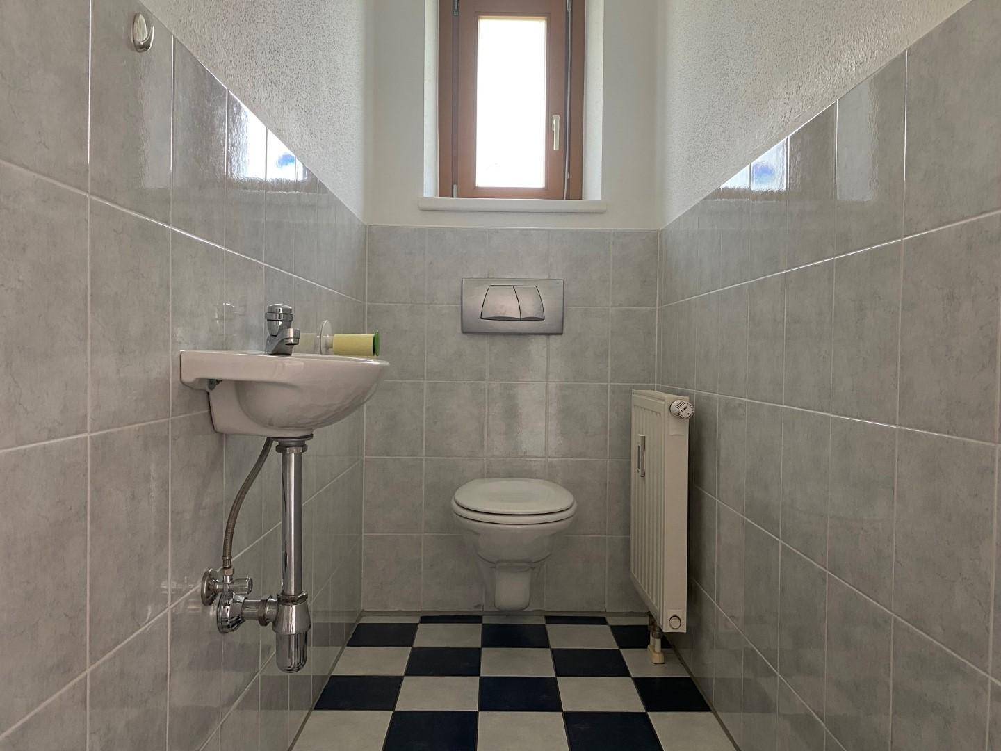 Kleines WC mit Fliesenboden, Wandfliesen und einem Fenster für Tageslicht.