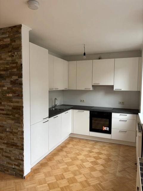 Moderne Küche mit weißen Schränken, dunklen Arbeitsplatten und integriertem Backofen.