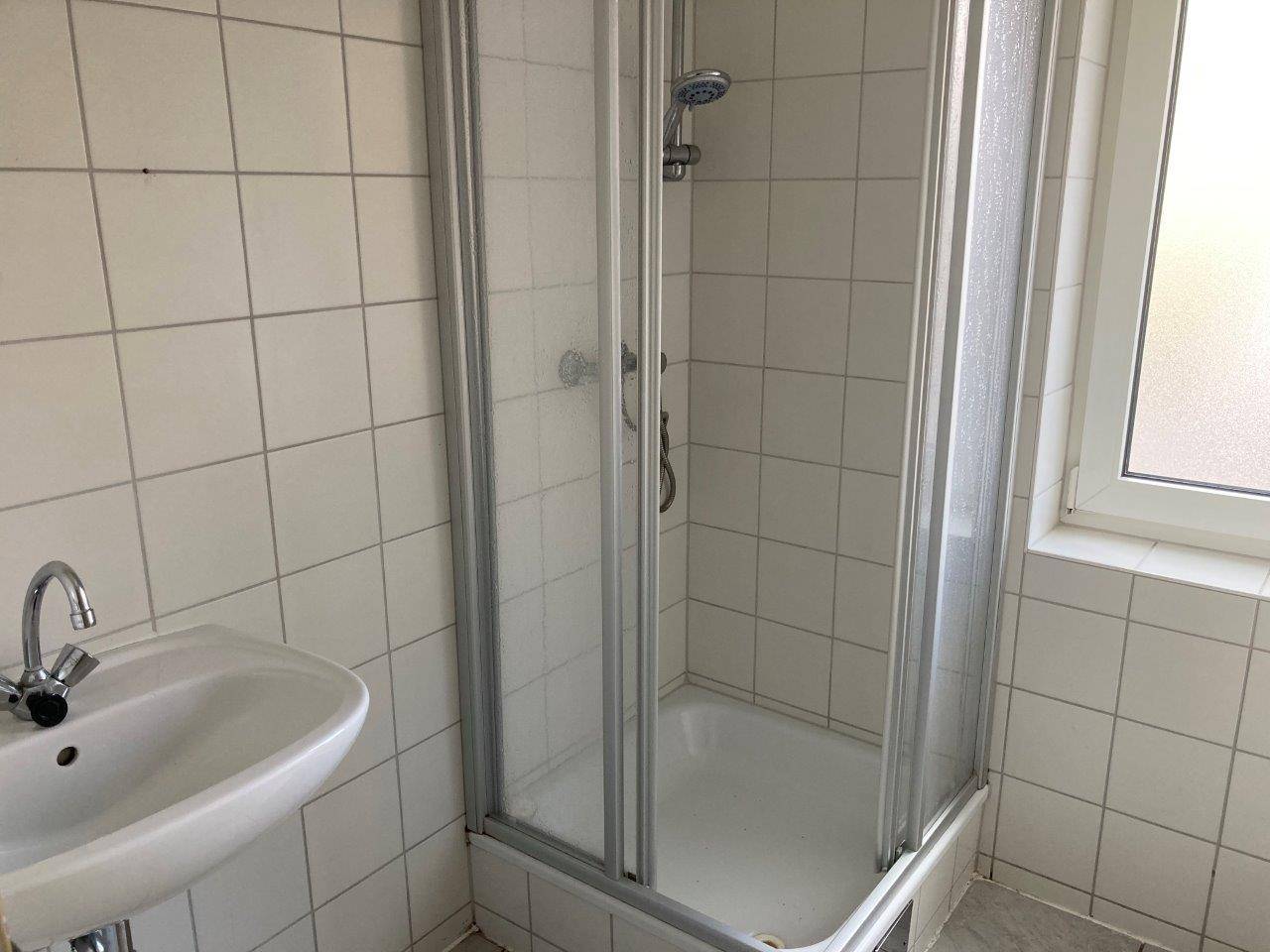 Funktionales Badezimmer mit Duschkabine, Waschbecken und Fenster für Tageslicht.