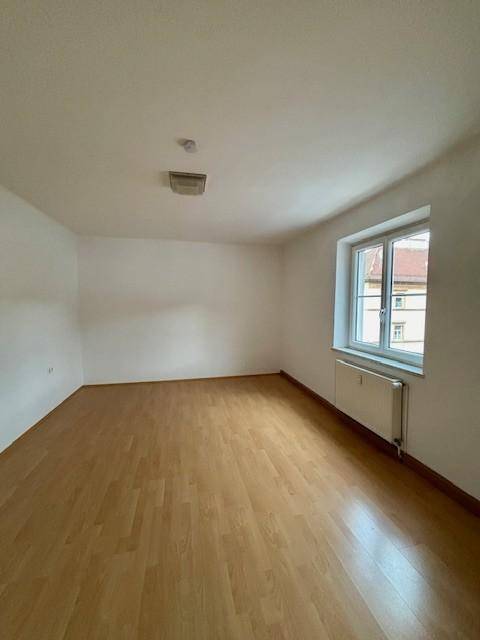 Geräumiges Zimmer mit hellem Laminatboden, weißen Wänden und einem großen Fenster.
