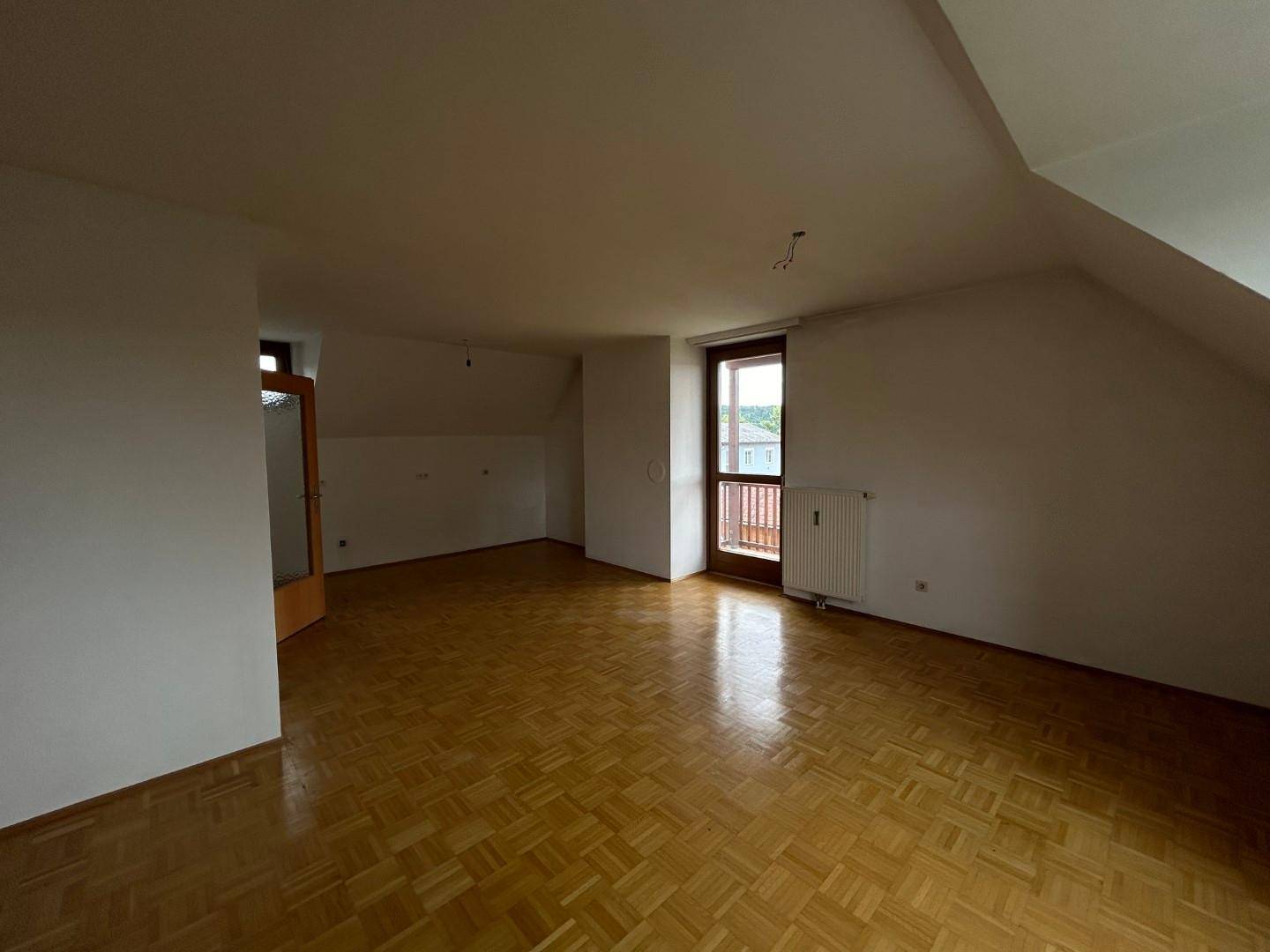 Heller Wohnraum mit Parkettboden, Dachschrägen und Zugang zu einem kleinen Balkon.