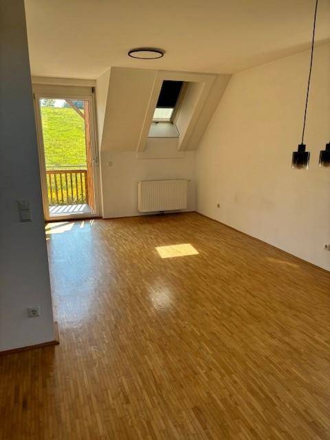 Geräumiges Wohnzimmer im Dachgeschoss mit Parkettboden, Dachfenster und Balkonzugang.