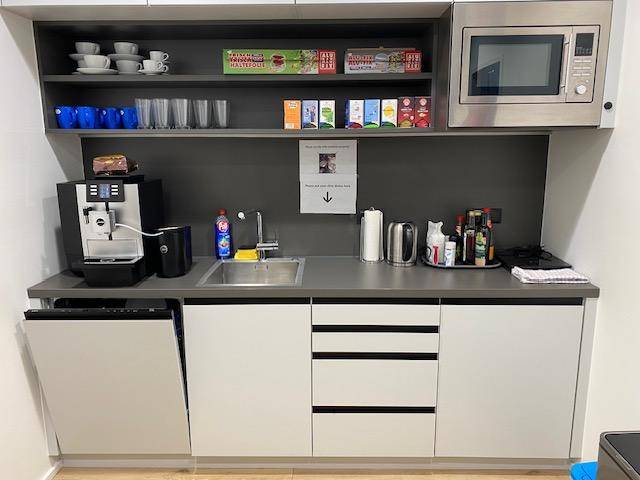 Kleine, funktionale Teeküche mit Spüle, Mikrowelle, Kaffeemaschine und integriertem Geschirrspüler.