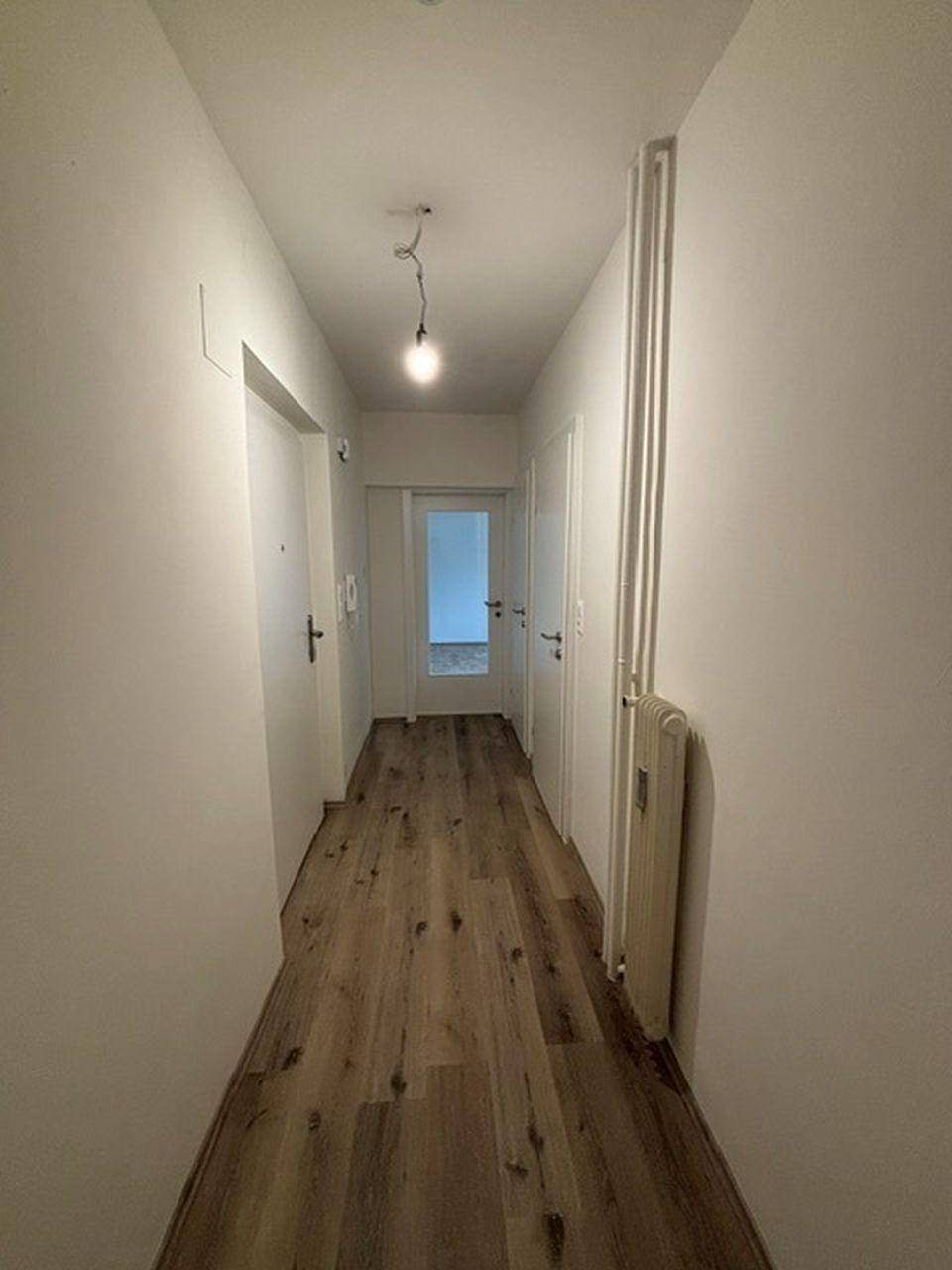 Langer, heller Flur mit Laminatboden und Heizkörper, der einen Zugang zu verschiedenen Zimmern bietet.
