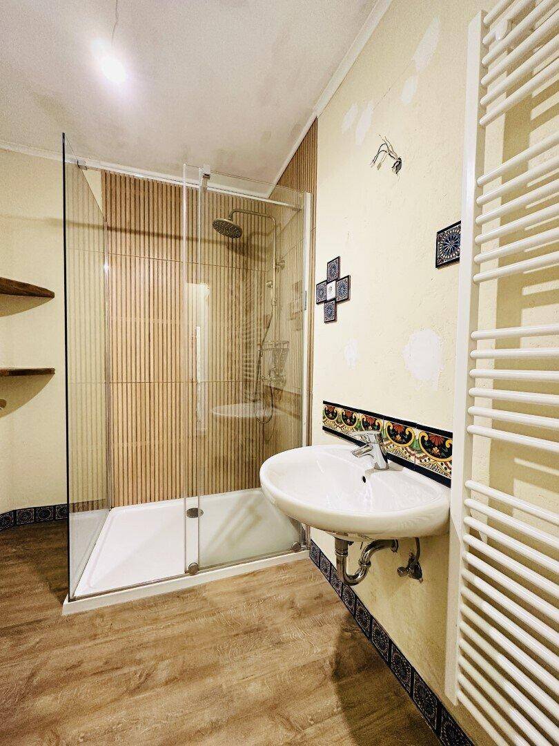 Modernes Badezimmer mit Duschkabine, Waschbecken und beheiztem Handtuchhalter.