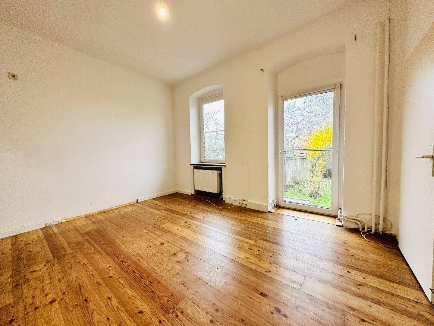 Geräumiger Raum mit Holzdielenboden und direktem Zugang zum Gartenbereich.