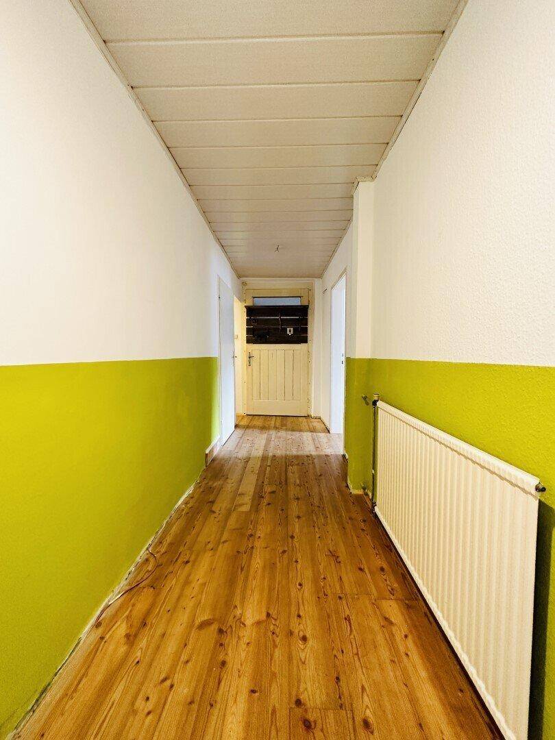 Langer Flur mit Holzdielenboden und einer auffälligen grünen Wandgestaltung.