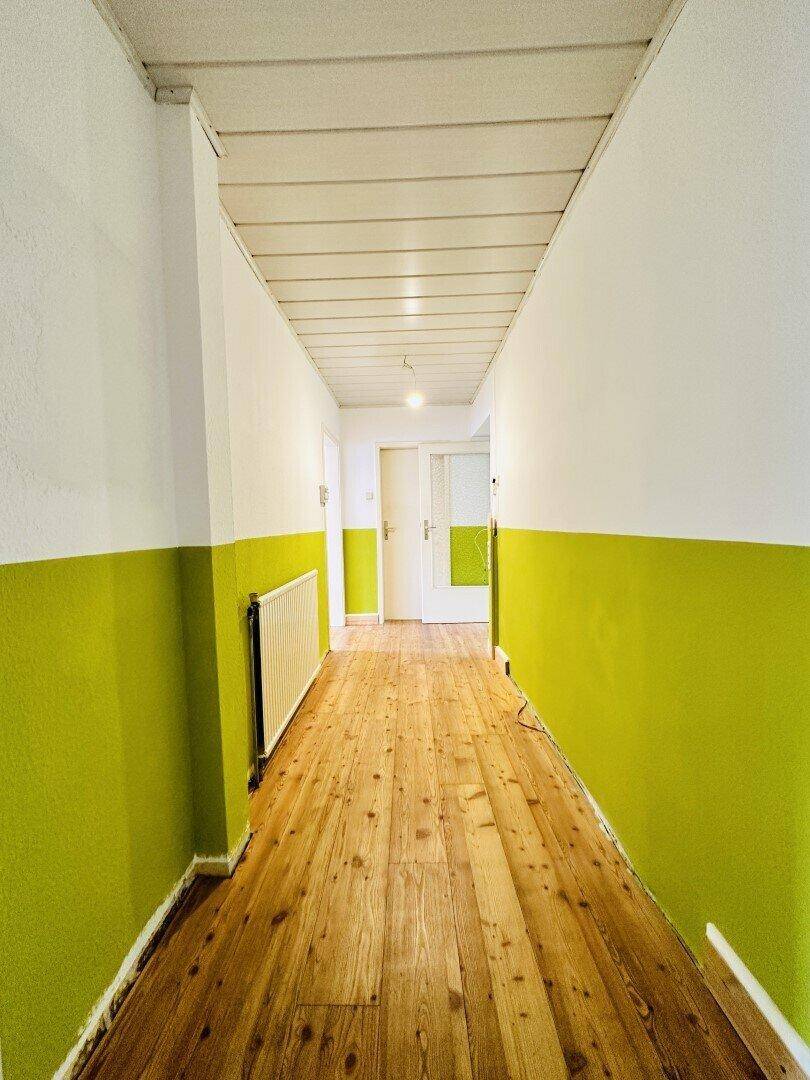 Heller Flur mit Holzdielenboden und einem Heizkörper an der Wand.