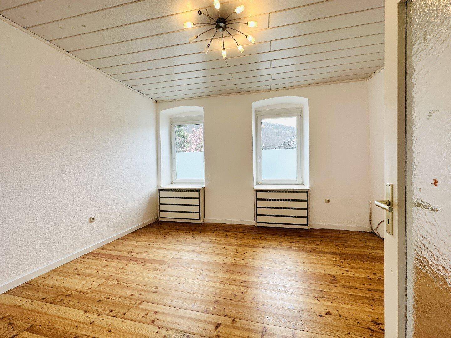 Helles Schlafzimmer mit Holzdielenboden und zwei Fenstern für viel Tageslicht.