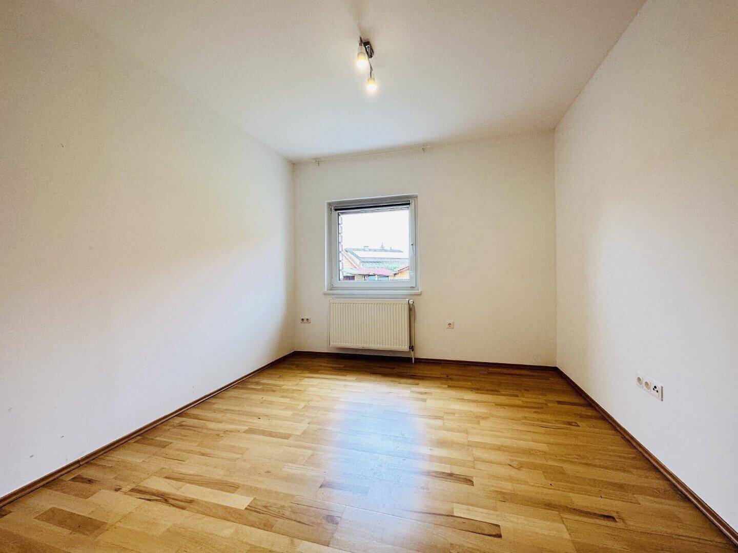 Gemütliches Schlafzimmer mit Laminatboden und einem Fenster, das Tageslicht hereinlässt.