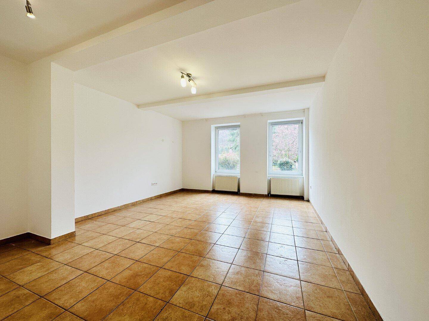 Geräumiges Wohnzimmer mit Terrakottafliesen und zwei Fenstern für eine helle Atmosphäre.