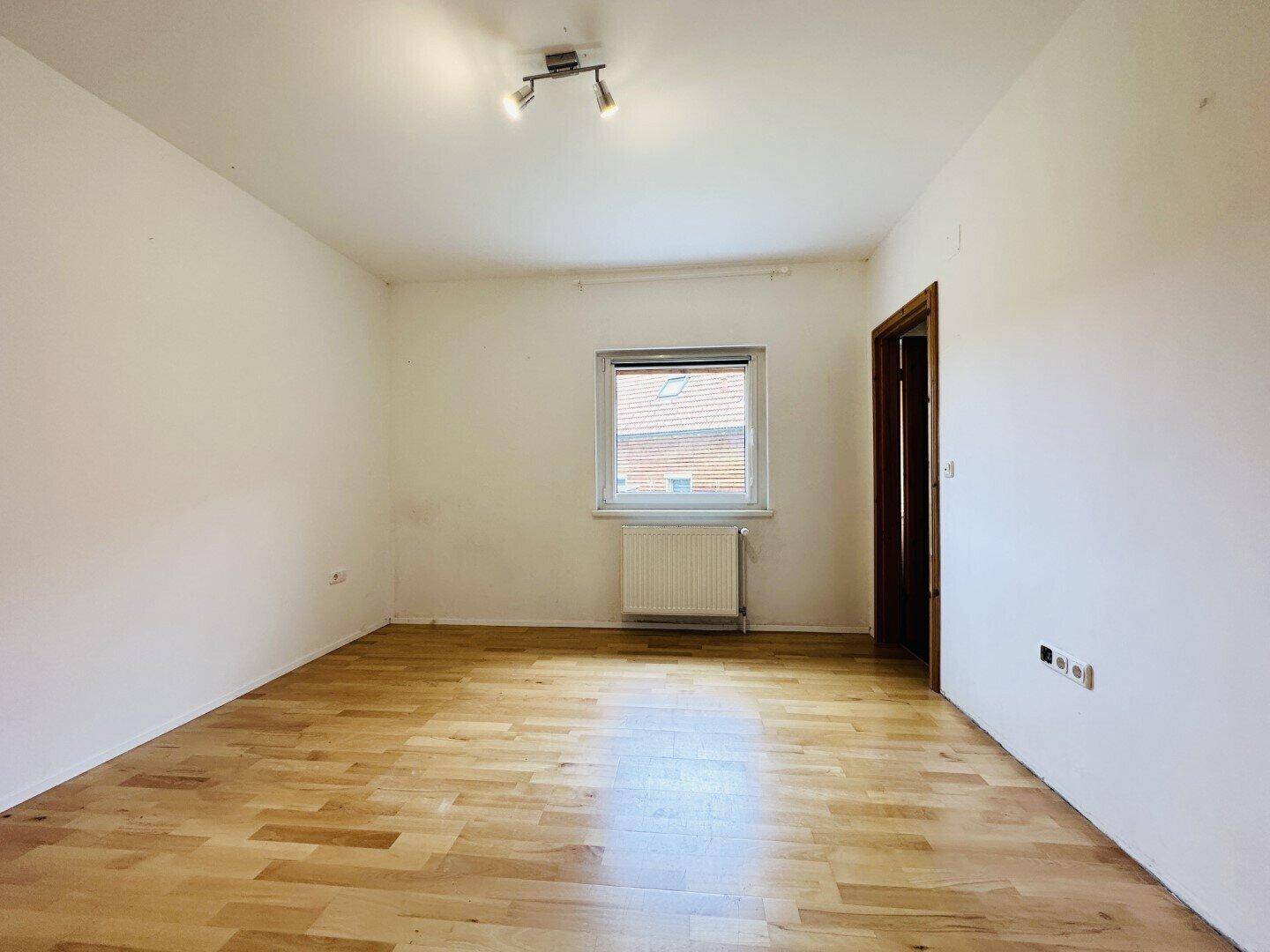 Helles Schlafzimmer mit Laminatboden und einem Fenster, das den Raum erhellt.