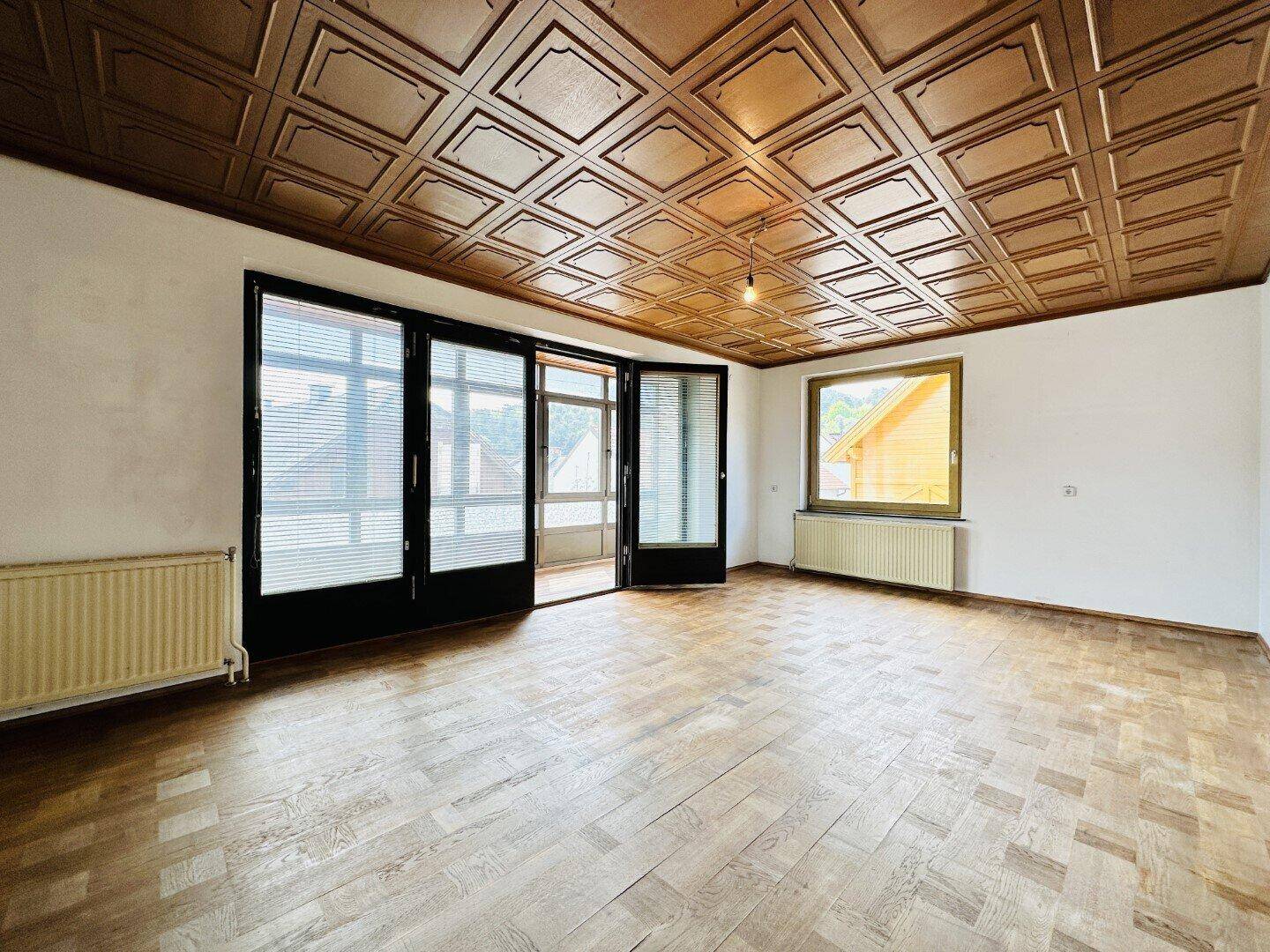 Helles Wohnzimmer mit Holzkassettendecke, Parkettboden und großen Fenstern.