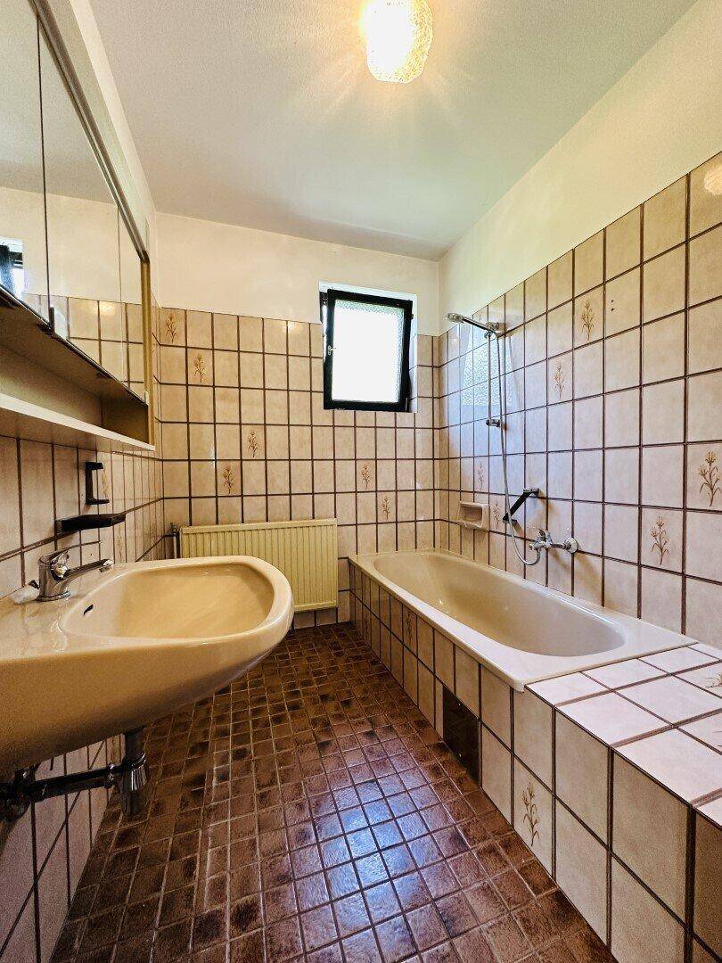 Badezimmer im 80er-Jahre-Stil mit Badewanne, Waschbecken und Fliesenboden.