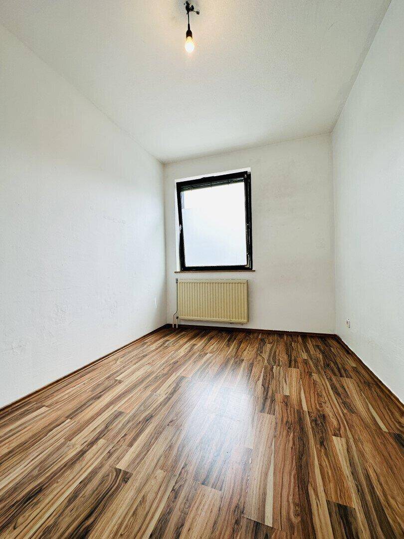 Helles, leeres Zimmer mit Laminatboden und einem Fenster, bereit zur individuellen Gestaltung.