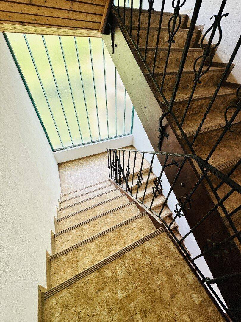 Helles Treppenhaus mit traditionellem schmiedeeisernem Geländer und großem Fenster für Tageslicht.