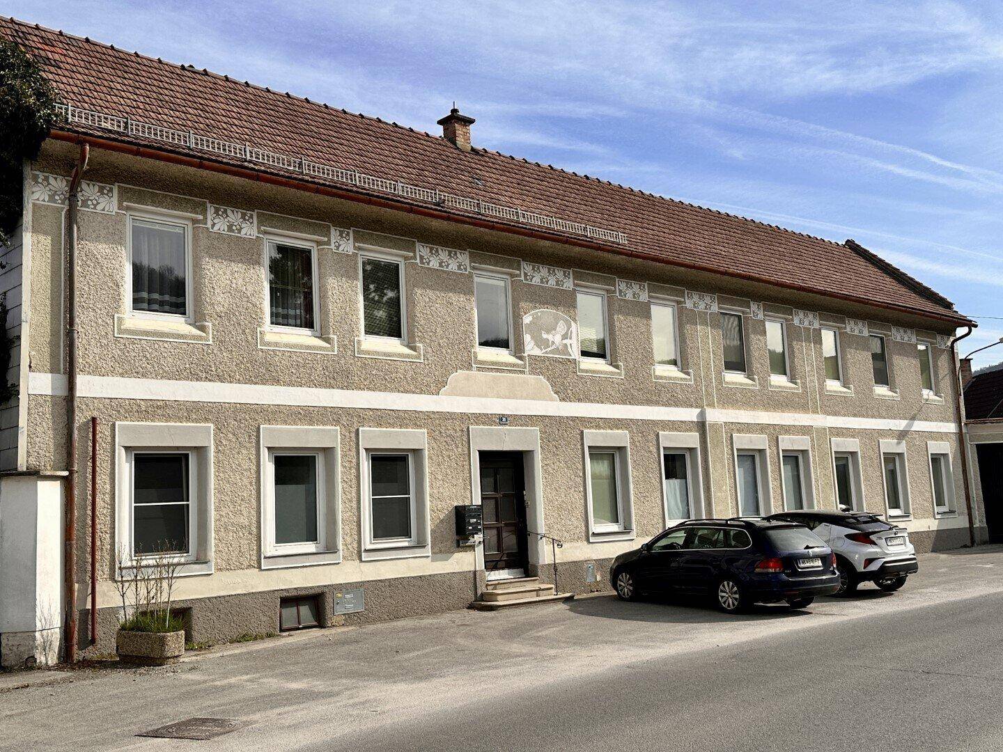Die Vorderseite des Gebäudes mit traditioneller Architektur und geparkten Fahrzeugen auf der Straße.