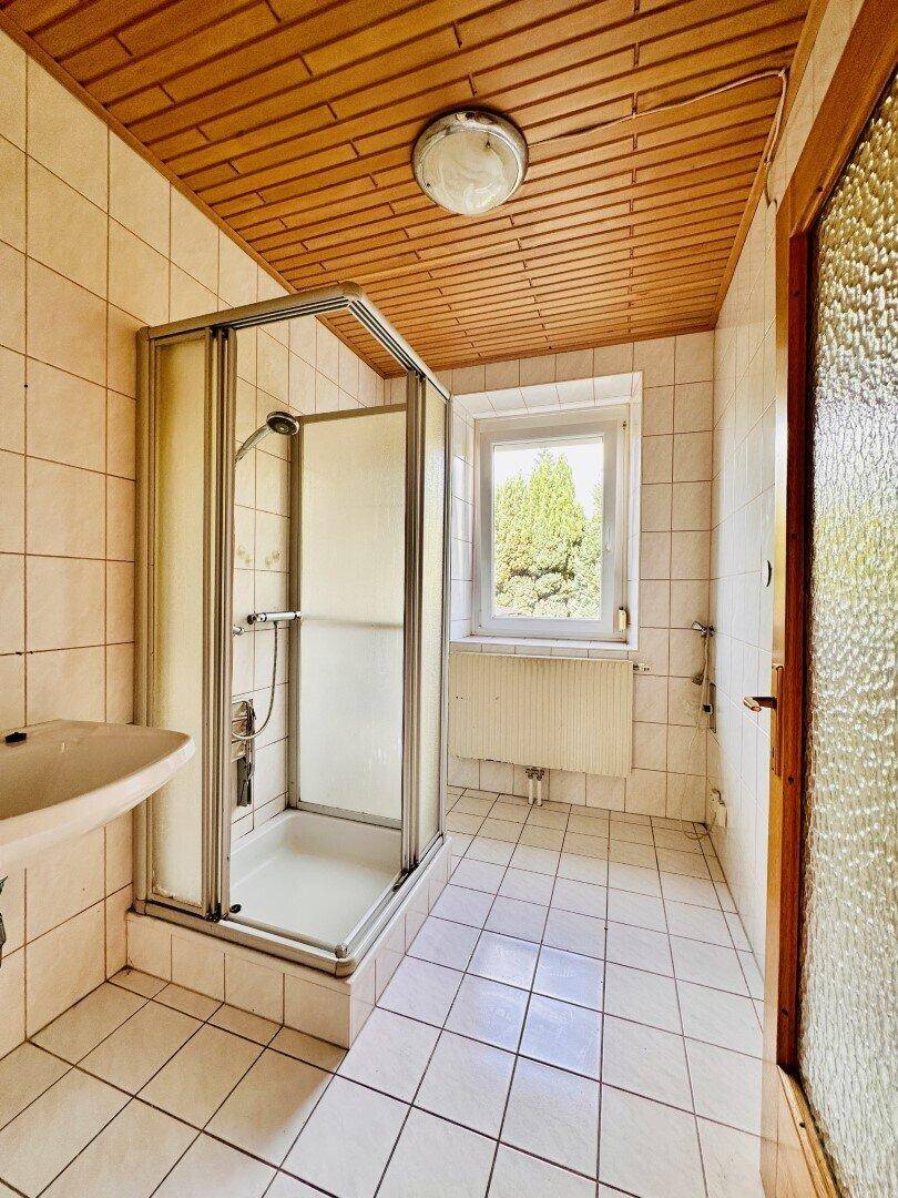 Badezimmer mit Duschkabine, Waschbecken, gefliesten Wänden und einer Holzdecke im Stil der 80er Jahre.