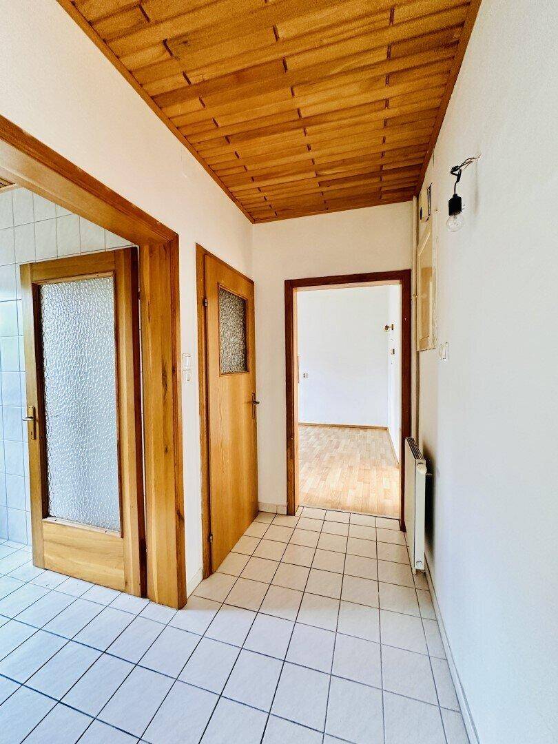 Flur mit Fliesenboden, Holztüren und einer Holzpaneeldecke, die zu verschiedenen Räumen führt.