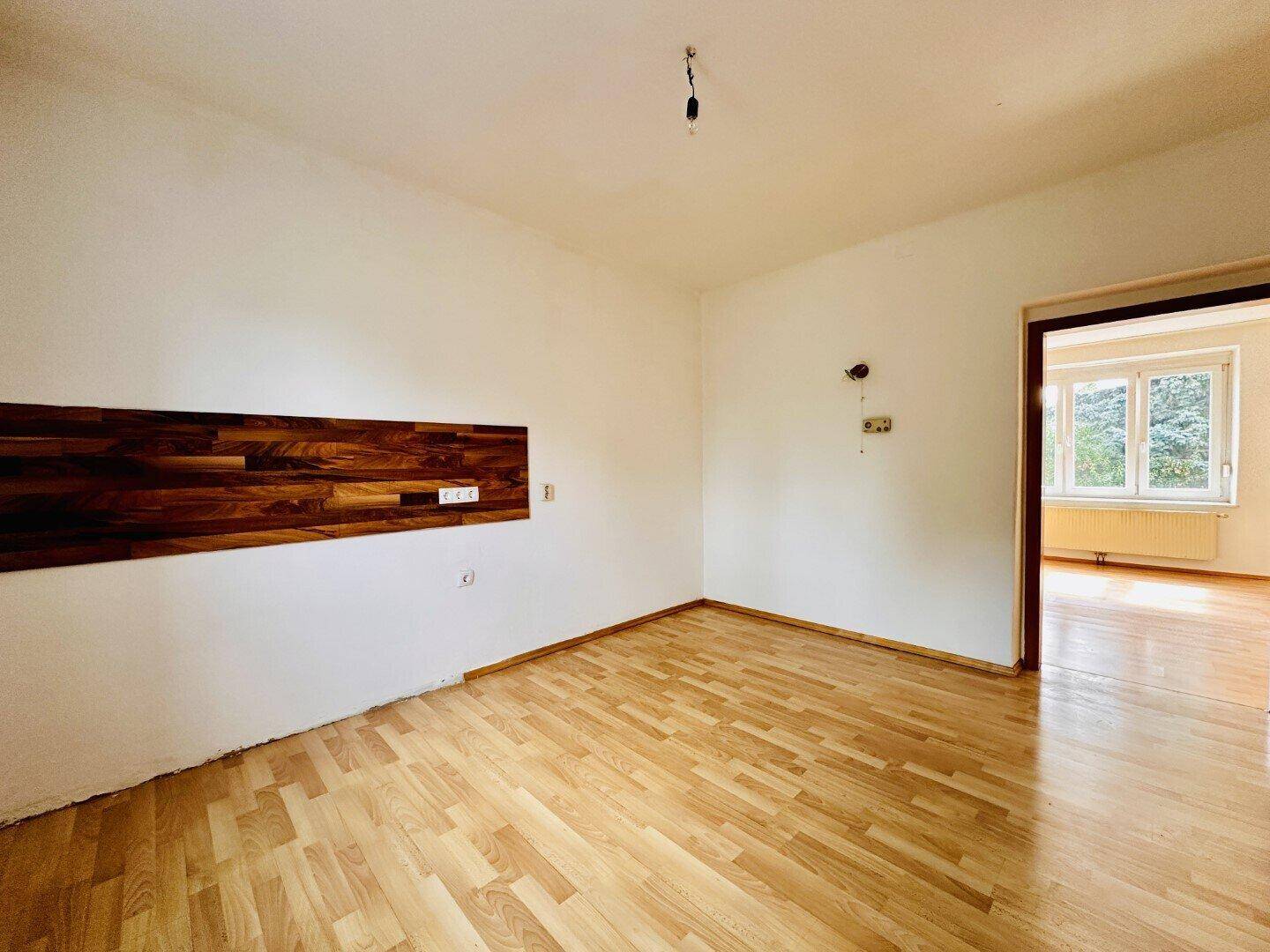 Geräumiges Zimmer mit Holzparkettboden und einer dekorativen Holzverkleidung an der Wand.