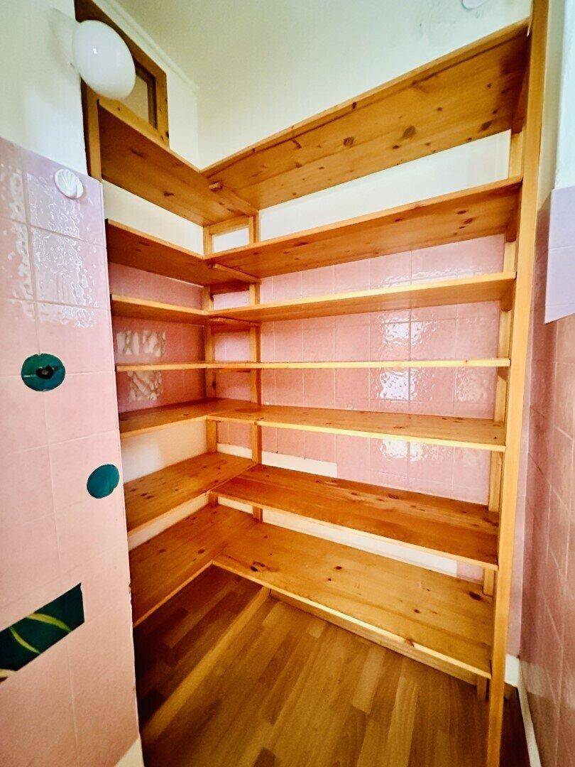 Praktische Speisekammer mit vielen Holzregalen und rosa Fliesen an den Wänden für zusätzlichen Stauraum.