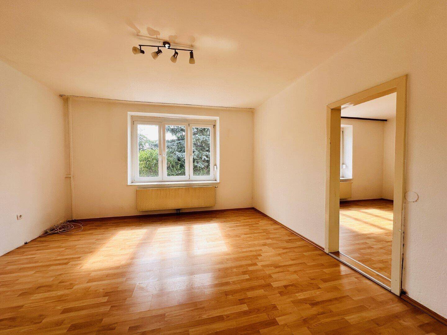 Sonniges Zimmer mit Holzparkettboden, großen Fenstern und viel natürlichem Licht.