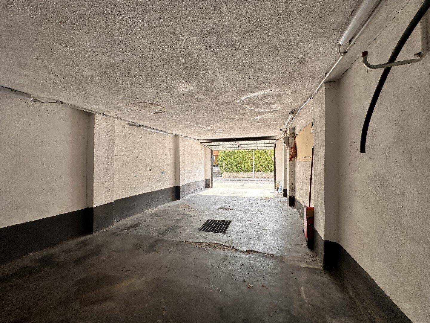 Geräumige Garage mit Betonboden und Zugang zum Außenbereich, ideal für Fahrzeuge.